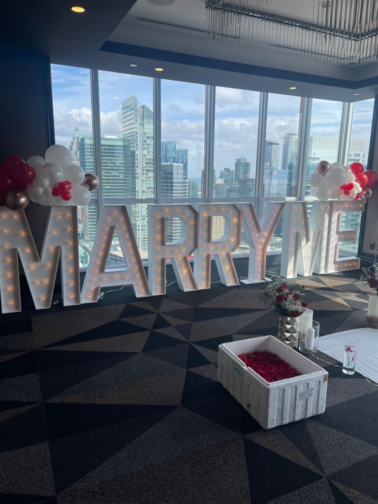 marquee letters that spell out "marry me," with balloon and flower decor